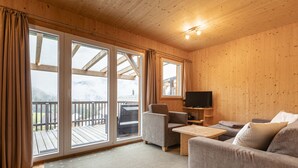 Ein Holzinnenraum mit einer Couch, einem Sessel und einem Fernseher auf einem Holztisch.