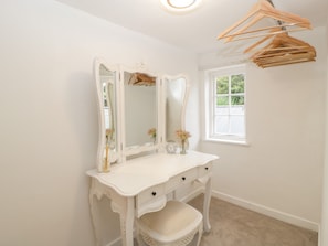 A white vanity with a mirror, a small table with flowers, and a window with a view. - 36 High Street (Salisbury)