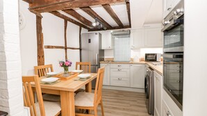 Une cuisine compacte avec des poutres en bois, une table à manger avec des chaises, un réfrigérateur, un four à micro-ondes et un lave-vaisselle.
