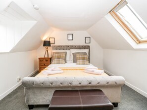 A bedroom with a bed, bedside table, lamp, and a bench. - 36 High Street (Salisbury)