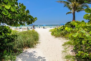 A sandy beach path leading to a beach with umbrellas and palm trees. - Townhome with Private Outdoor Living Space, Community Pool - Sea La Vie (Holmes Beach)
