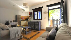 Een woonkamer met een bank, een klein tafeltje, een kast en een raam met uitzicht op een hek en palmbomen.