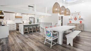 A modern kitchen with white cabinetry, a central island with stools, and a dining area with a white table and bench. - Private Pool | LSV | 2 Min Walk to Beach (Santa Rosa Beach)