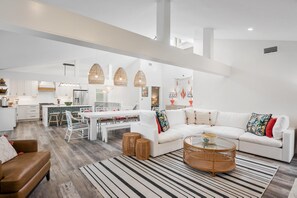 Un salón amplio con un sofá blanco, una mesa de comedor y una cocina al fondo.