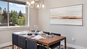 A dining area with a wooden table, chairs, and a view of trees through a large window.
