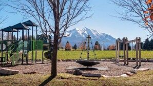 A playground with a climbing structure, swings, and a slide, set against a backdrop of a mountain.
