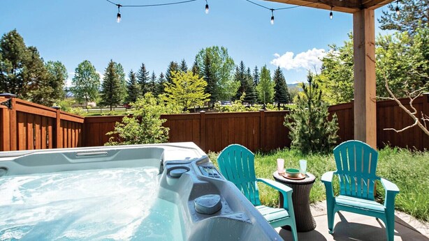 A hot tub with two chairs and a table, surrounded by a wooden deck and a wooden fence.