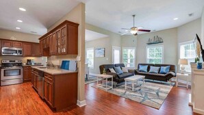 A spacious living area with a kitchen, wooden cabinets, a dining table, and a sofa. - Buckroe Beach Home with King Bed, Grill, Games and 5 min Walk to Beach…Sleeps 8. (Hampton)