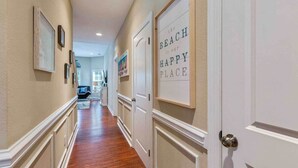 A hallway with wooden flooring, white doors, and framed artwork on the walls. - Buckroe Beach Home with King Bed, Grill, Games and 5 min Walk to Beach…Sleeps 8. (Hampton)
