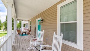 A covered porch with white chairs and a table, beige siding, and a large window. - Buckroe Beach Home with King Bed, Grill, Games and 5 min Walk to Beach…Sleeps 8. (Hampton)