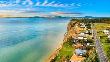 An aerial view of a coastal area with a road, houses, and a clear view of the ocean.