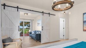 Une chambre avec un grand lit, une porte coulissante de style grange, une vue sur l’extérieur et un lustre.