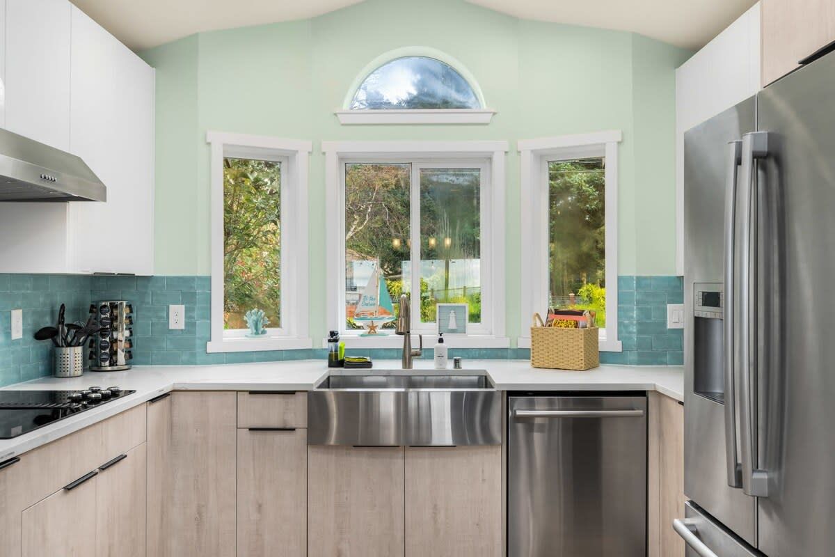 A modern kitchen with a central island, stainless steel appliances, and a view through large windows.