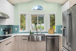 A modern kitchen with a central island, stainless steel appliances, and a view through large windows.