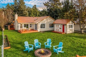 Ein zweistöckiges Haus mit roter Tür, einer Laube und einer Feuerstelle mit vier blauen Adirondack-Stühlen.