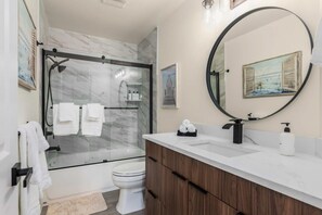 A modern bathroom with a glass-enclosed shower, a white toilet, and a wooden vanity with a large mirror. - @ Marbella Lane – Wave HS w/EV Charger, Oceanfront! (Oak Harbor)
