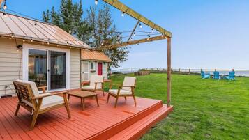 A wooden deck with outdoor furniture, a covered area with string lights, and a view of a grassy yard with chairs.