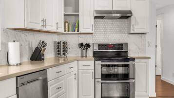 A modern kitchen with white cabinets, a stainless steel dishwasher, a double oven, and a hexagonal tile backsplash.