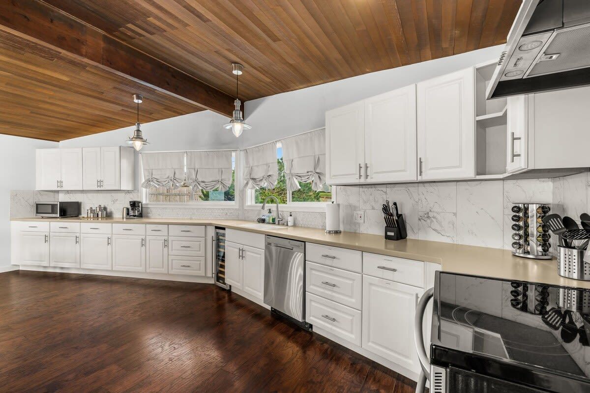 Una cocina moderna con armarios blancos, techo de madera y un ventanal grande.
