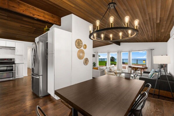 A modern kitchen with a large island, stainless steel appliances, and a dining area with a dark wood table and chairs.