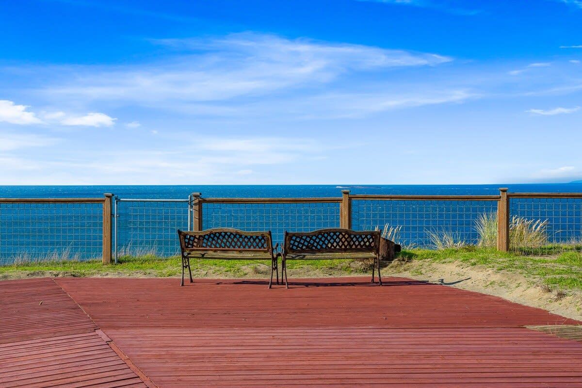 Una terraza de madera con dos bancos que dan a una playa.