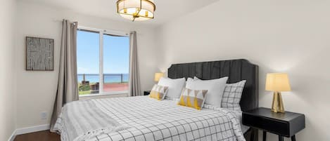 A bedroom with a bed, nightstands, a chandelier, a window with curtains, and a view of the outdoors.