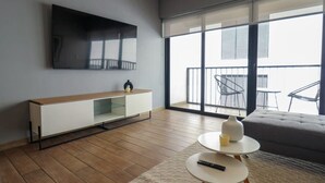 Un soggiorno moderno con una TV a schermo piatto, un tavolino consolle in legno, un divano grigio e un balcone con mobili da esterno.