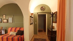 Ett vardagsrum med en färgglad randig soffa, en liten matta och en hall som leder till en dörr.