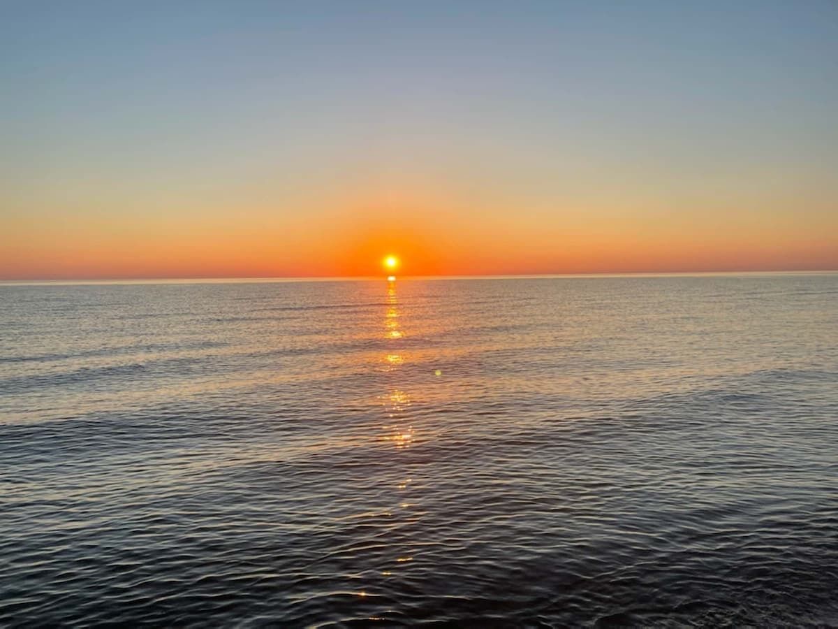Un coucher de soleil sur une mer calme, sans terre ni constructions visibles à l’horizon.