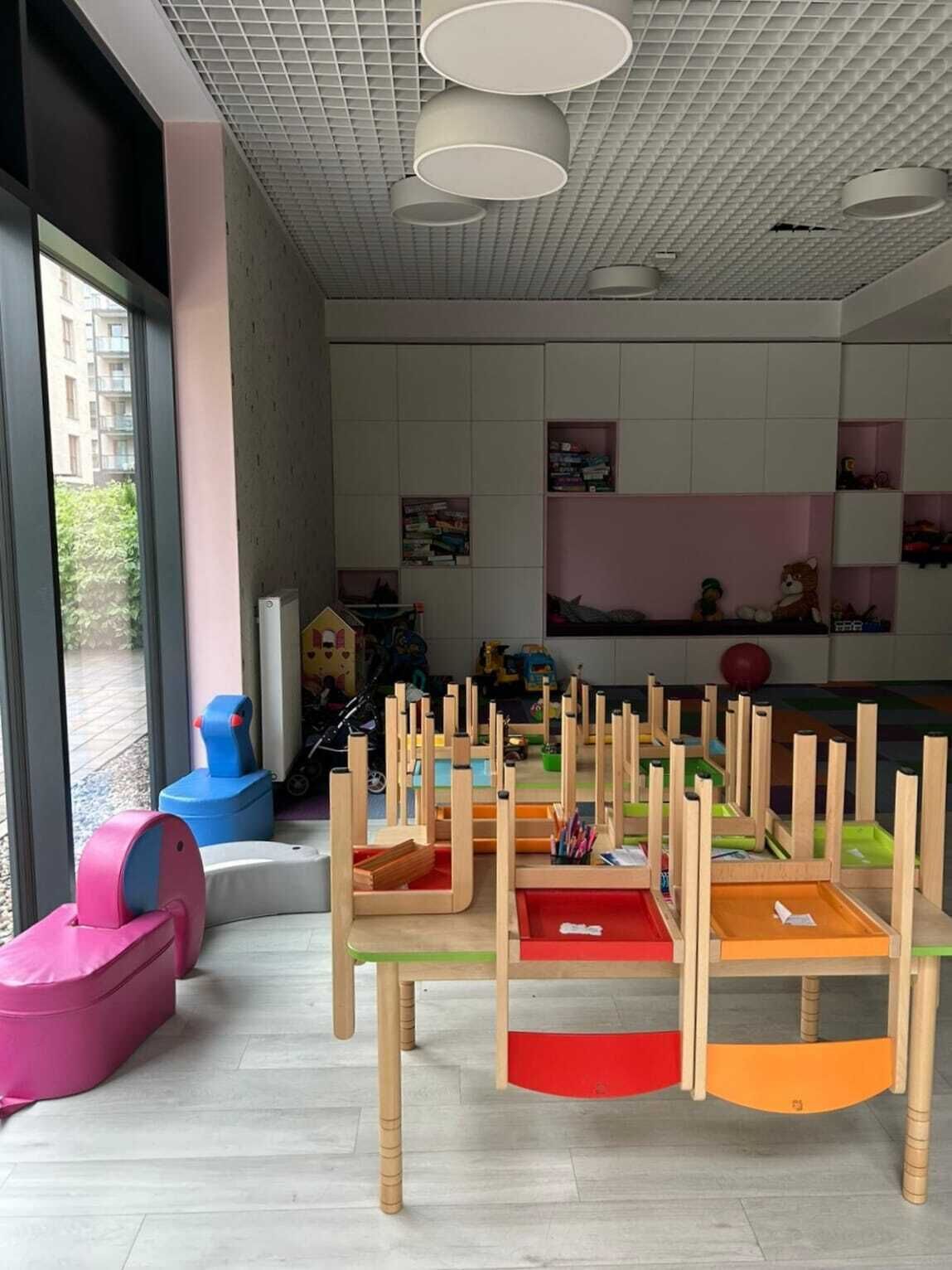 A children's play area with colorful play structures and a large window providing a view of the outside.