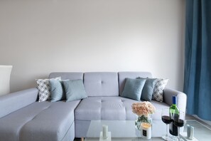 Een moderne woonkamer met een grijze modulaire bank, een glazen salontafel en een vaas met bloemen.