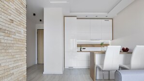 Cozinha moderna com armários brancos, bancada de madeira e área de refeições com cadeiras brancas.