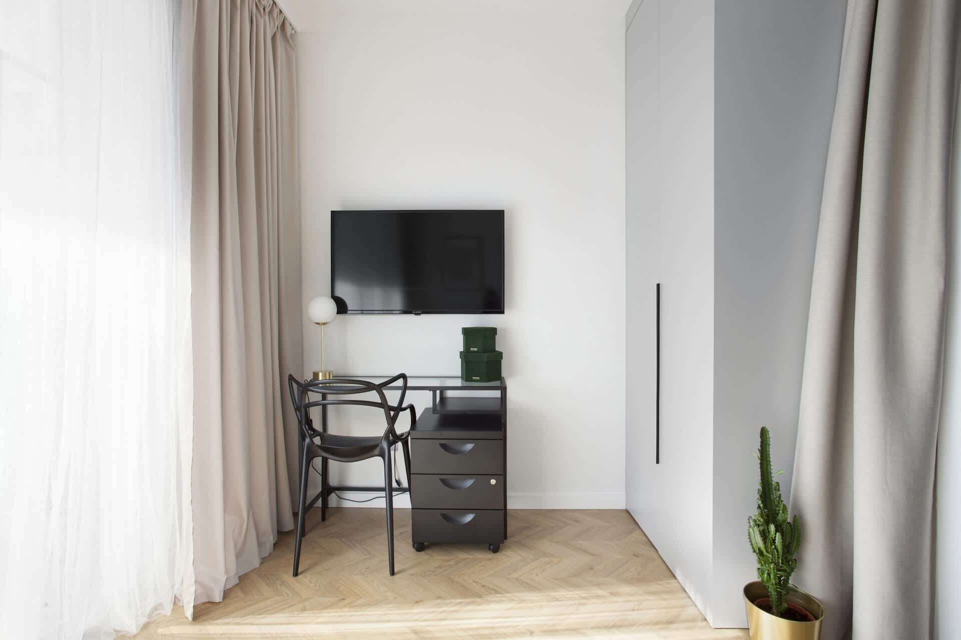 Une petite pièce moderne équipée d’un bureau, d’une chaise et d’un téléviseur fixé au mur.