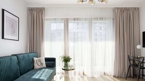 Sala de estar moderna com um sofá azul-turquesa, uma mesinha lateral com um vaso, cortinas leves e vista para a cidade.