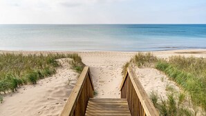 Une promenade en bois mène à une plage de sable fin bordée d’une eau d’un bleu limpide.