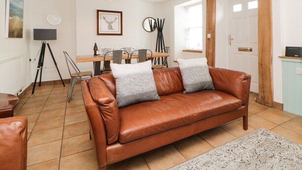 A cozy living room with a brown leather sofa, a dining table with chairs, a tripod lamp, and a framed deer picture on the wall. - The Yellow House, 13 King Street (Dawlish)