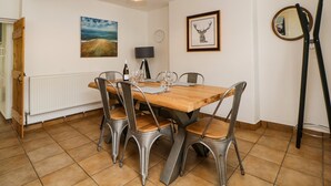A dining room with a wooden table, metal chairs, a pendant light, a painting, a framed deer head, and a mirror. - The Yellow House, 13 King Street (Dawlish)