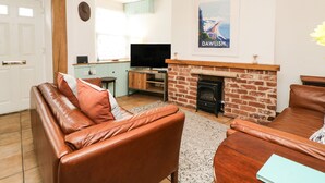 A living room with a fireplace, leather sofas, a television, and a 'DAWLISH' poster on the wall. - The Yellow House, 13 King Street (Dawlish)