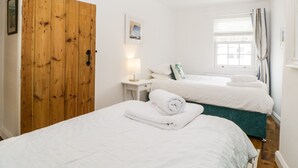 A bedroom with two beds, a wooden door, a bedside table with a lamp, and a window with curtains. - The Yellow House, 13 King Street (Dawlish)