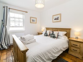Una cama bien hecha con sábanas blancas y almohadones decorativos, un cabecero de madera, una lámpara de noche y un cuadro en la pared.
