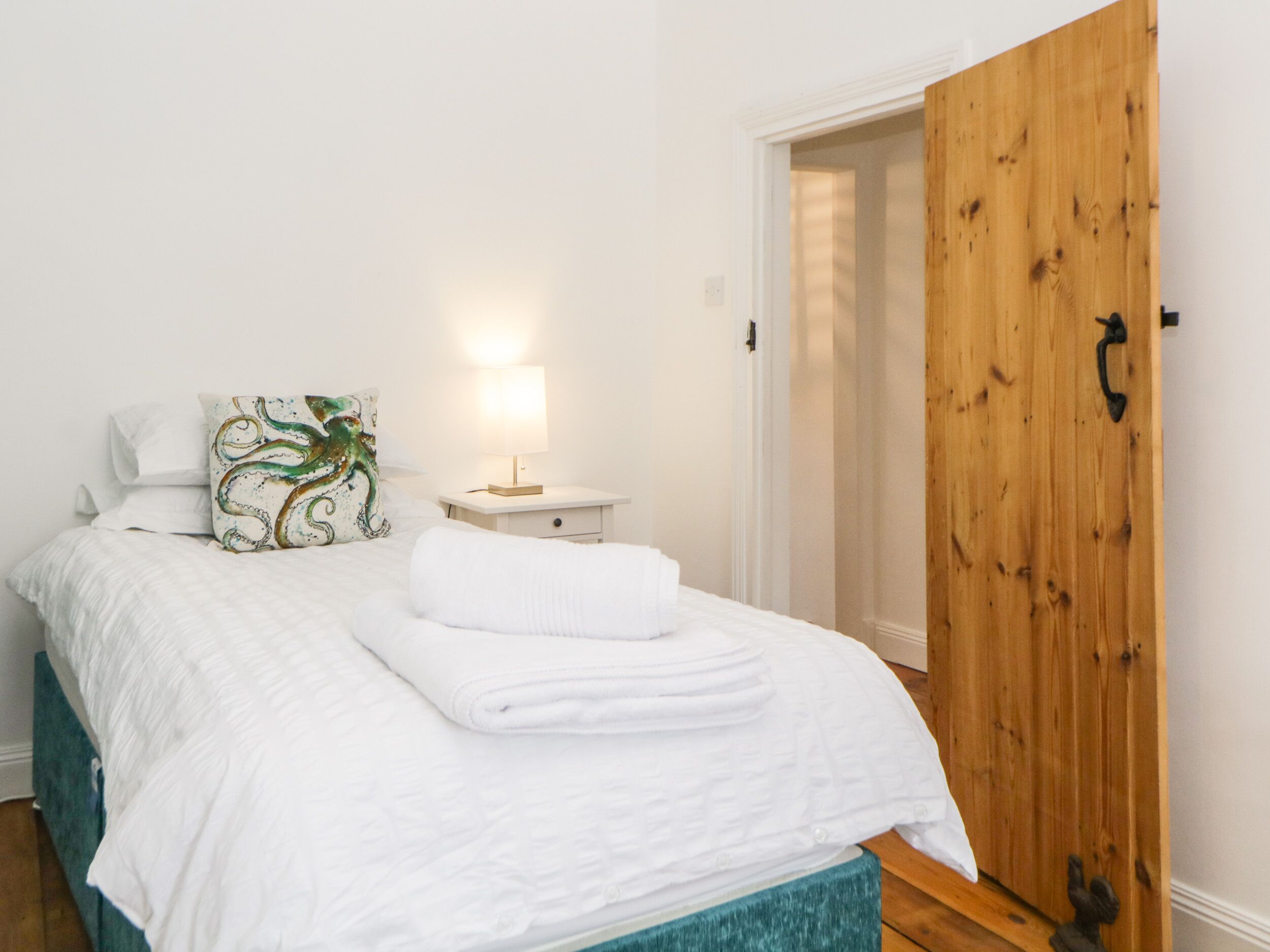 Un dormitorio con cama, mesita de noche, lámpara, armario de madera y una puerta.