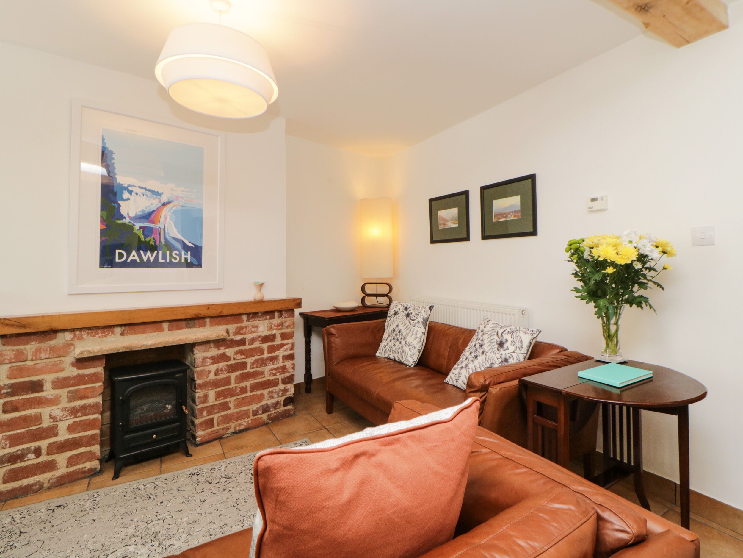 A living room with a brick fireplace, leather sofa, and a small table with a vase of flowers.