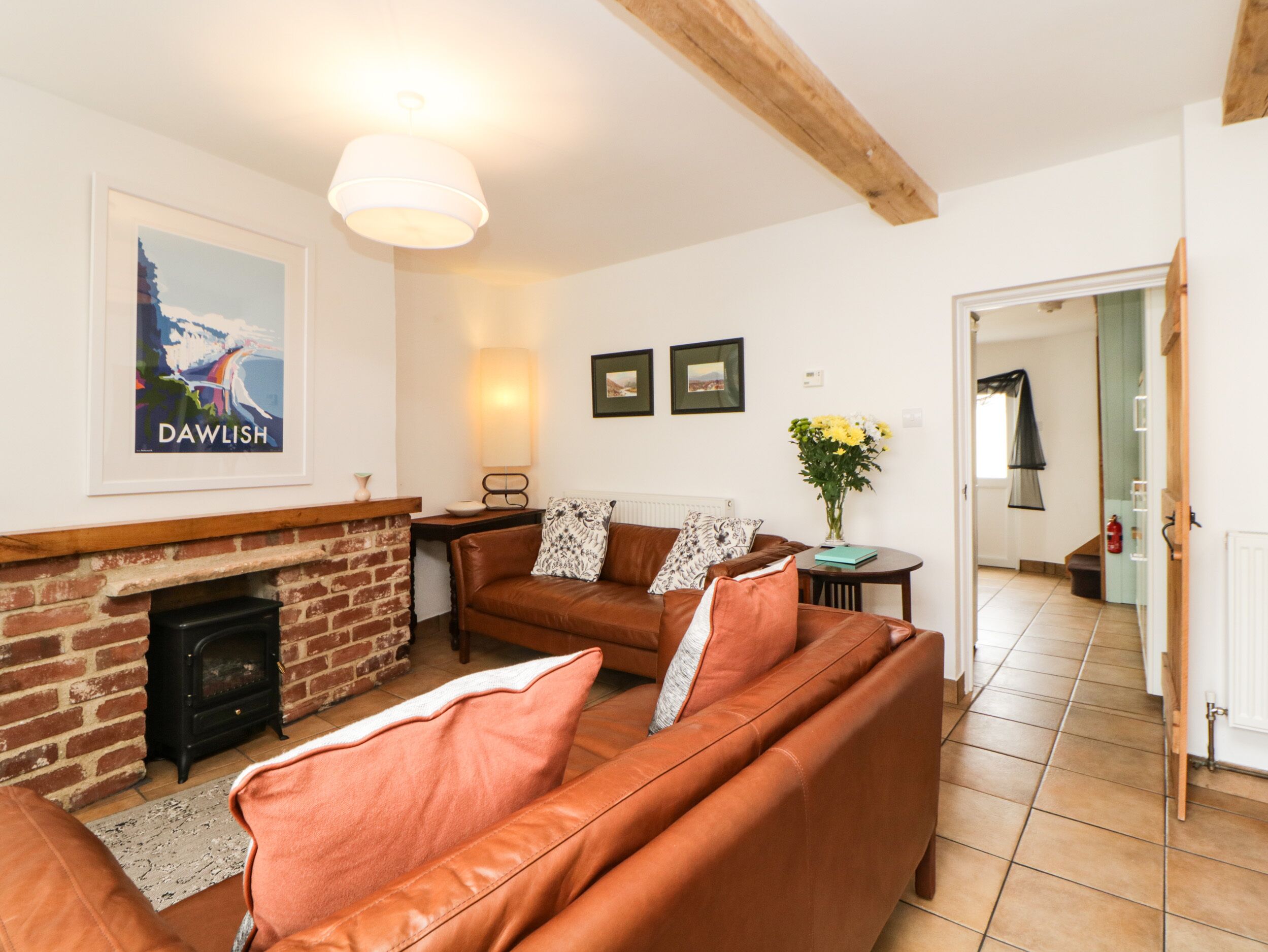 A living room with a brick fireplace, a brown leather sofa, a table with a lamp, and framed pictures on the wall.