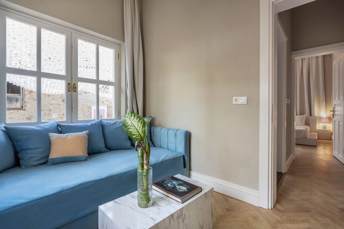 A modern living room with a blue sofa, a marble coffee table, and a vase with a plant.