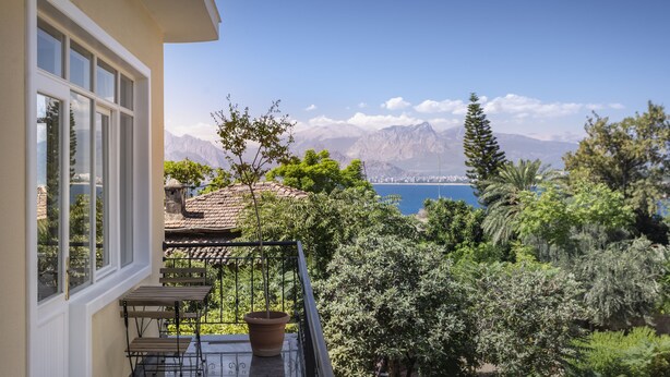 A balcony with a table and chairs, overlooking a mountainous landscape and a body of water. - House of Good Things (Antalya)