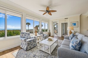 A spacious living room with large windows, a ceiling fan, and a view of the ocean.