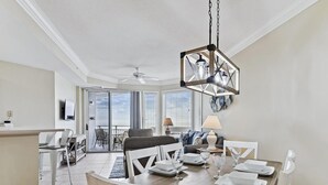 A dining area with a wooden table set for four, a ceiling fan, and a view of the balcony. - Enjoy 5th Floor Views of the Ocean & Amenities (Hilton Head Island)