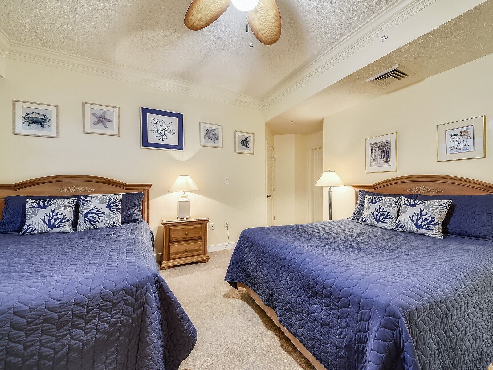 A hotel room with two beds, a nightstand, a lamp, and framed artwork on the walls.
