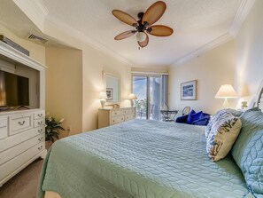 A bedroom with a bed, a ceiling fan, a dresser, a television, and a balcony with a view.