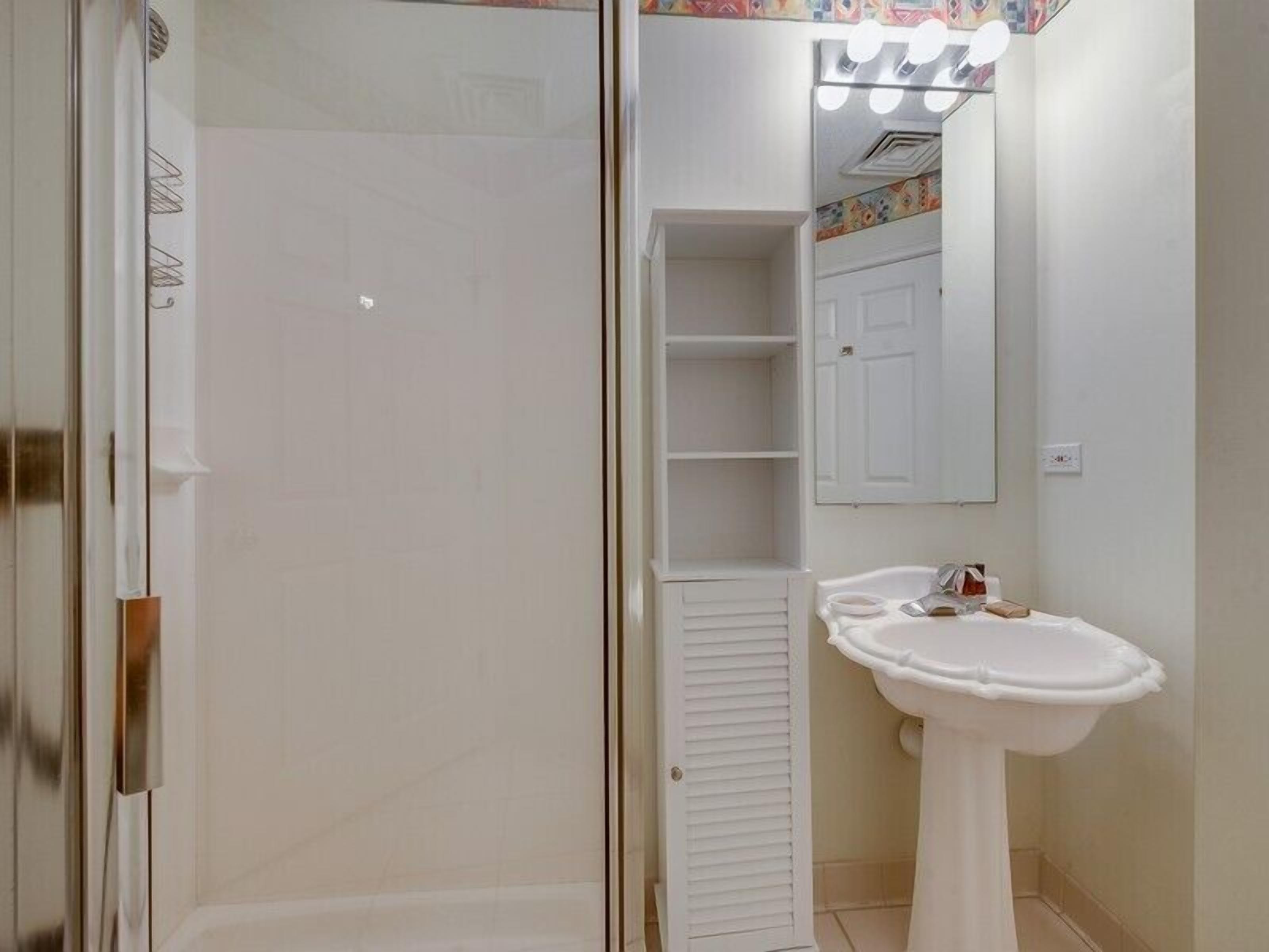 A bathroom with a glass shower enclosure, a pedestal sink, and a vanity with a mirror.